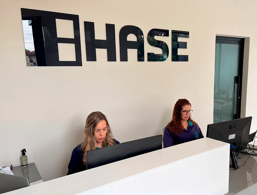 Recepção do escritório da HASE, com duas atendentes trabalhando sob o letreiro da marca na parede.