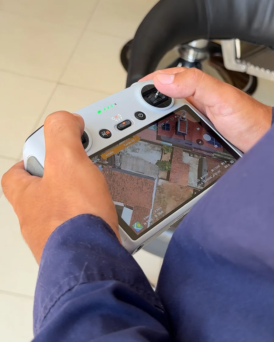 Técnico da HASE segurando o controle do drone, com a imagem aérea do telhado na tela.